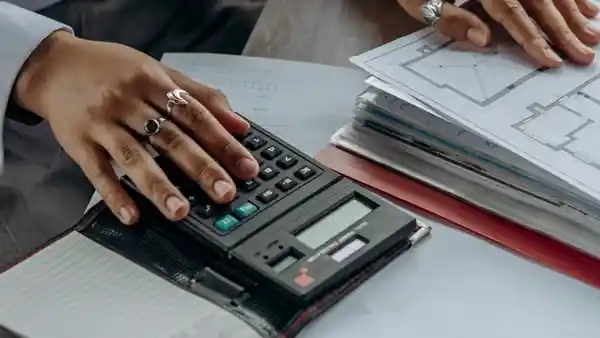 Hands using a calculator beside printed plans and notes.
