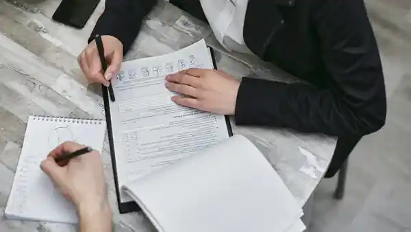 Two people at a table annotating a printed form and a notebook.