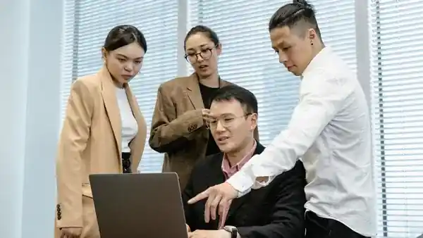 Four colleagues learning together around a laptop.